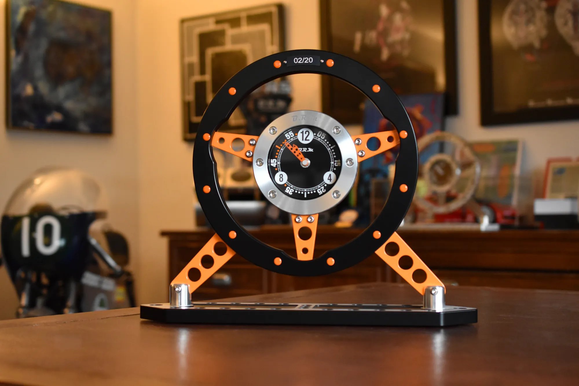Le Volant, anodisation noire et rayons orange, posé sur une commode en bois dans un bureau